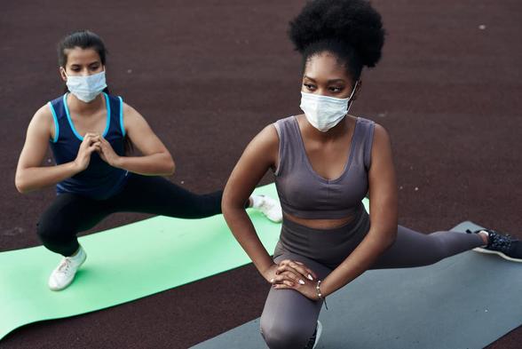 Two people doing yoga wearing facemasks.