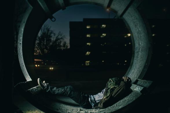 A man sleeping in a tunnel with his face covered.