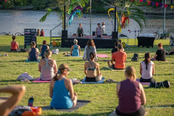 A group of people in exercise clothes doing yoga on a green grass field by the water.