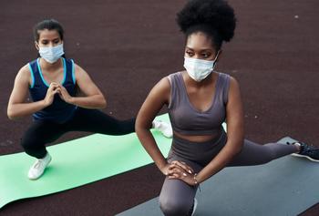 Two people doing yoga wearing facemasks.