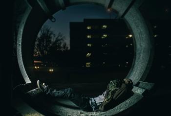 A man sleeping in a tunnel with his face covered.