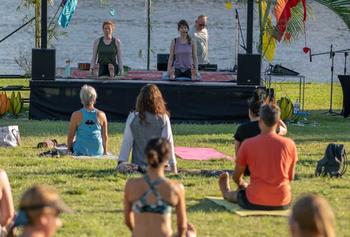A group of people in exercise clothes doing yoga on a green grass field by the water.