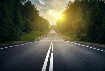 Image of empty road leading into early morning light in the distance