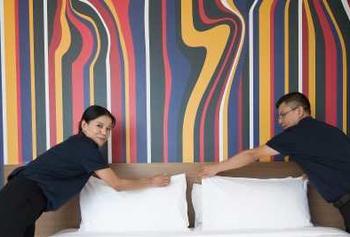 Two people changing sheets on a bed.